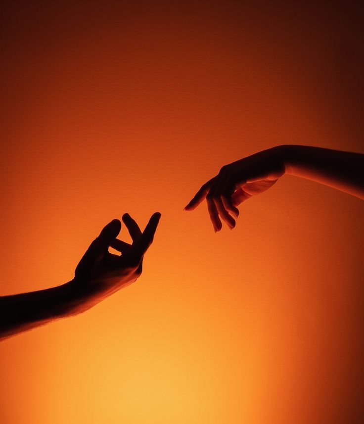 Two hands reaching towards each other with one hand outstretched, lit with orange lighting for an emotional touch.